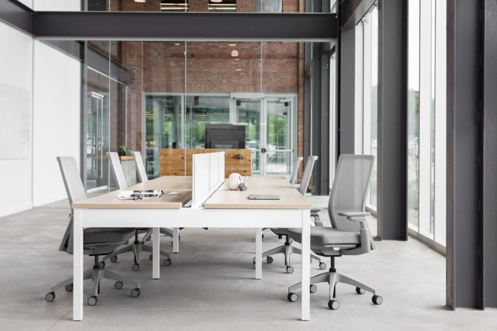 Ergonomic office chairs around a conference table in a bright, modern workspace with glass walls and.