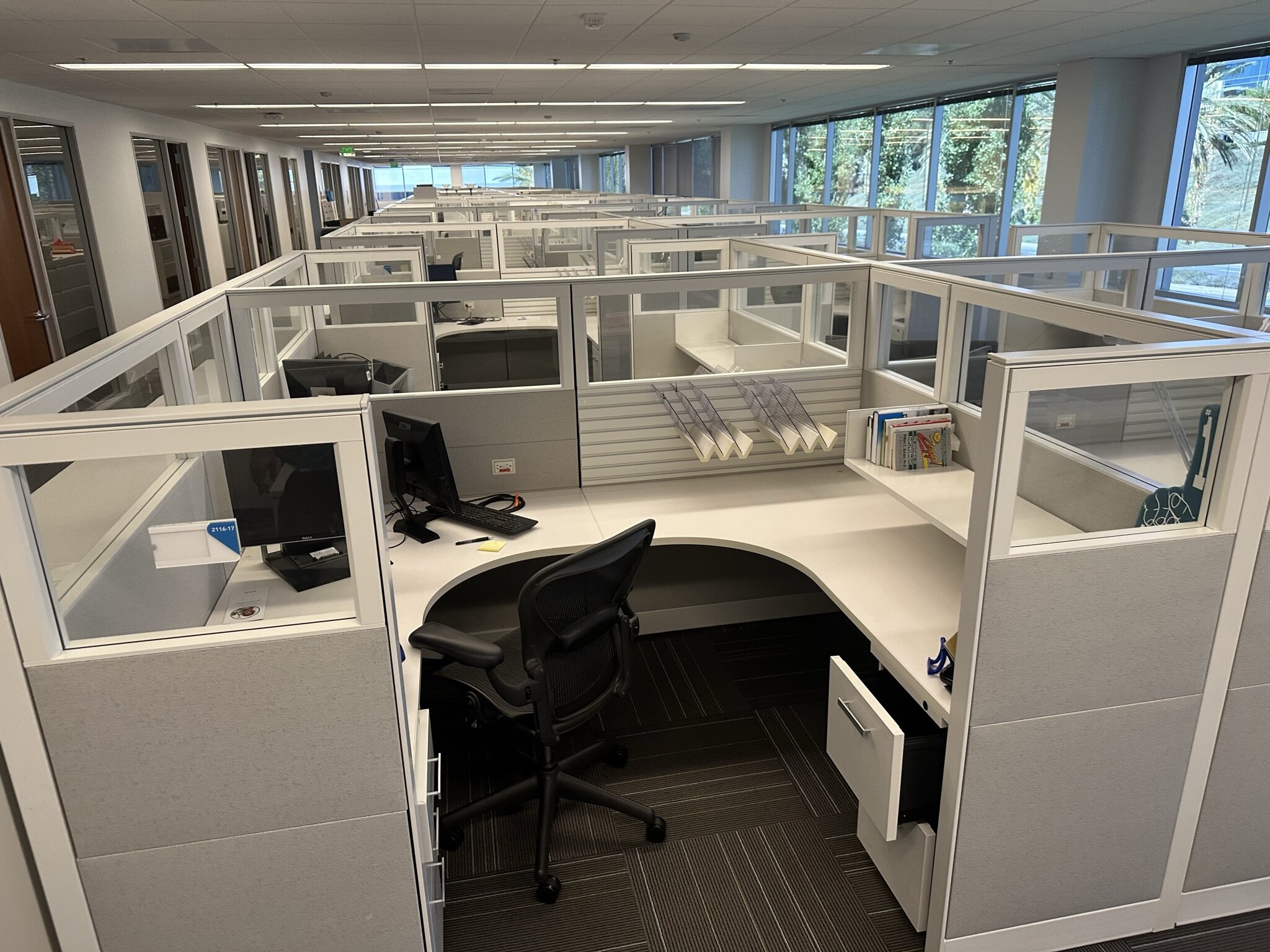 Office cubicles with glass partitions and ergonomic chairs at liquidation sale.