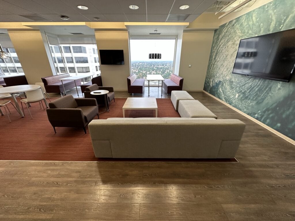 Spacious office lounge featuring contemporary furniture, large windows, and scenic cityscape views.