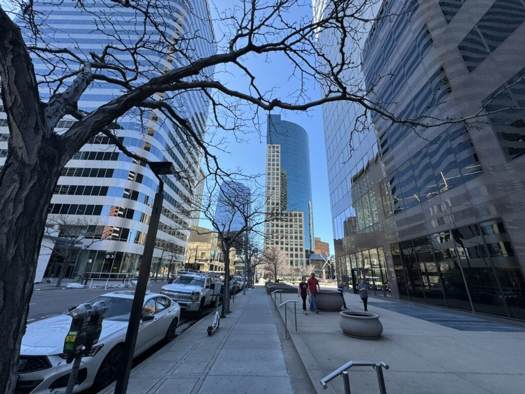 Urban cityscape with tall buildings, busy sidewalk, and clear blue sky.