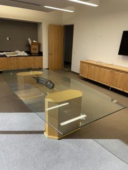 Office conference table with glass surface and wooden legs for professional meeting spaces.