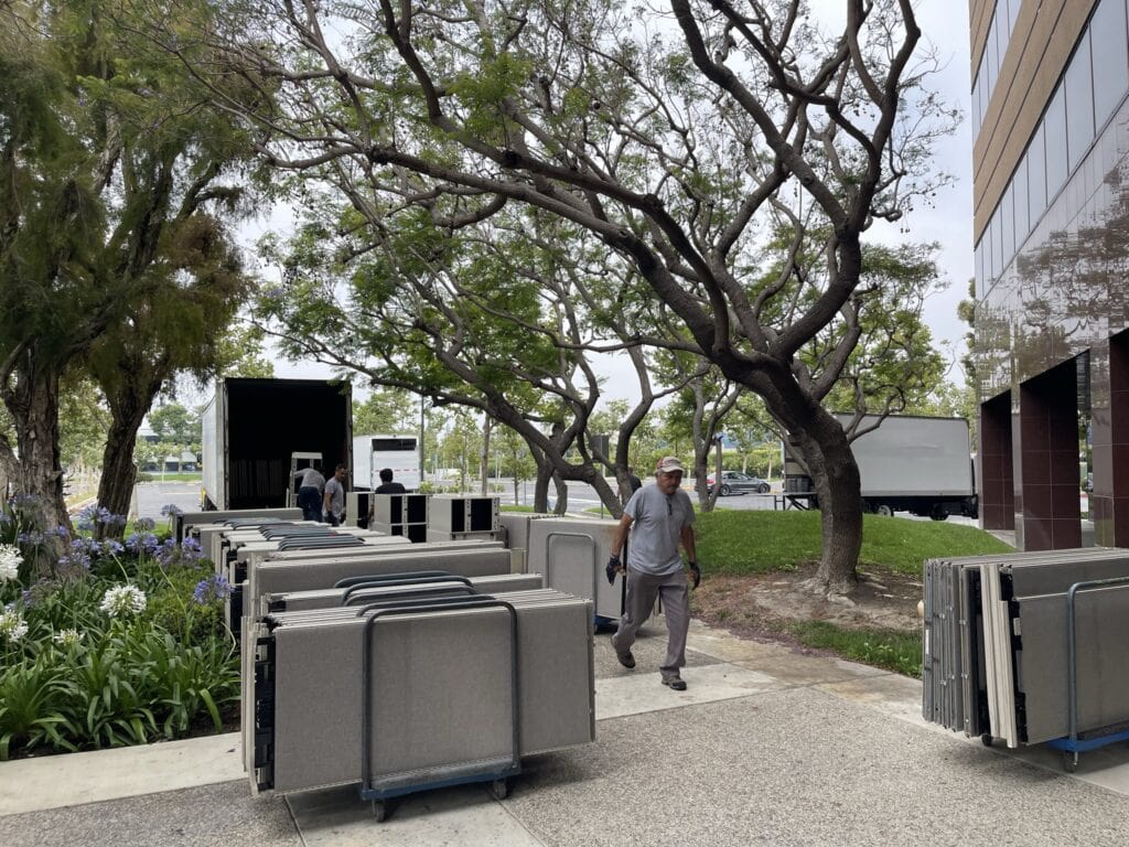 Pre-owned office cubicles and furniture being arranged outdoors for liquidation sale.