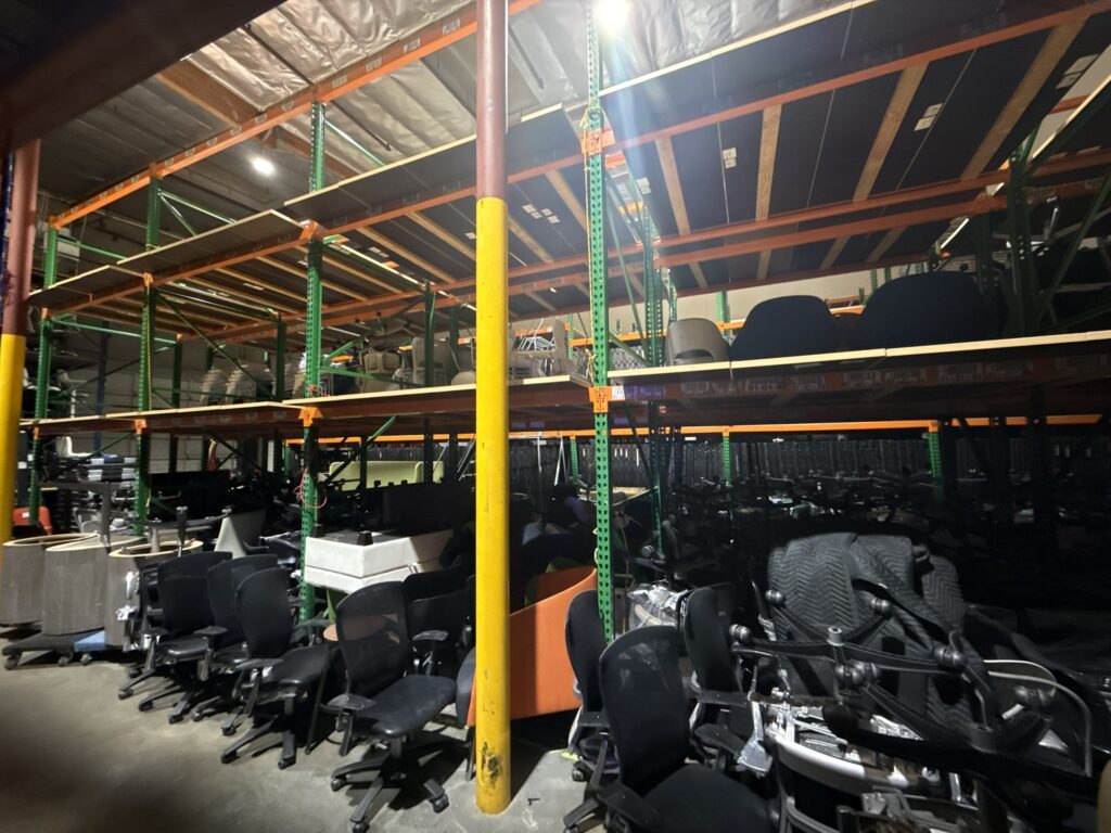 Office furniture storage in a warehouse with shelving units and chairs.