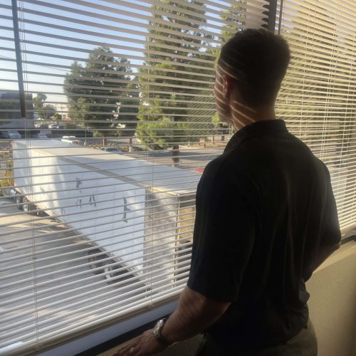 Man looking out window at trucks, commercial vehicle dealership, Cube World USA.